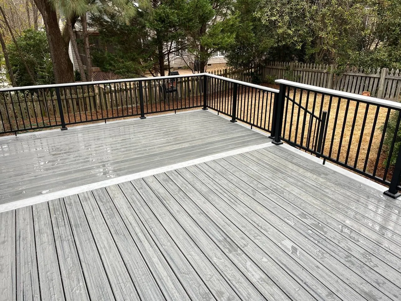 Wide grey composite deck with black aluminium railing overlooking a wooded backyard