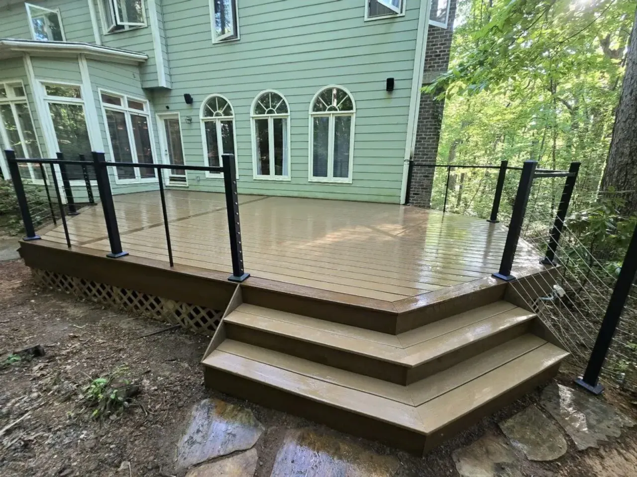Composite deck with black cable railing and wide cascading steps behind a sage-green Triangle home