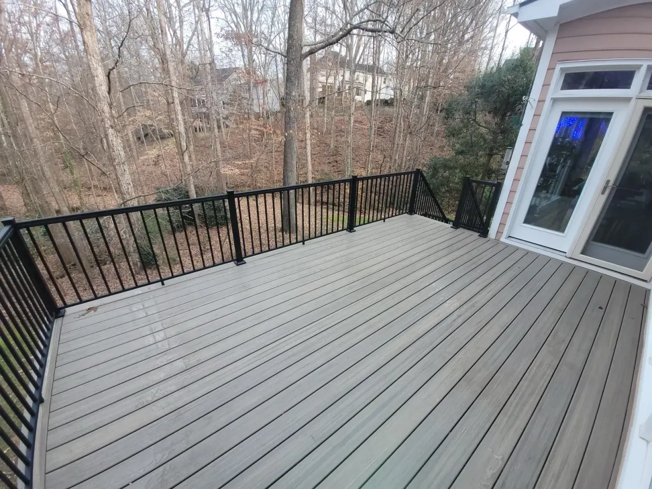 Grey composite deck with black aluminium railing overlooking a wooded backyard
