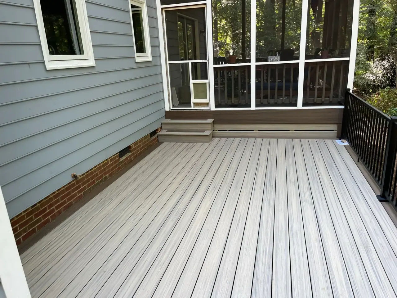 Wide composite deck running along gray siding beside a screened porch