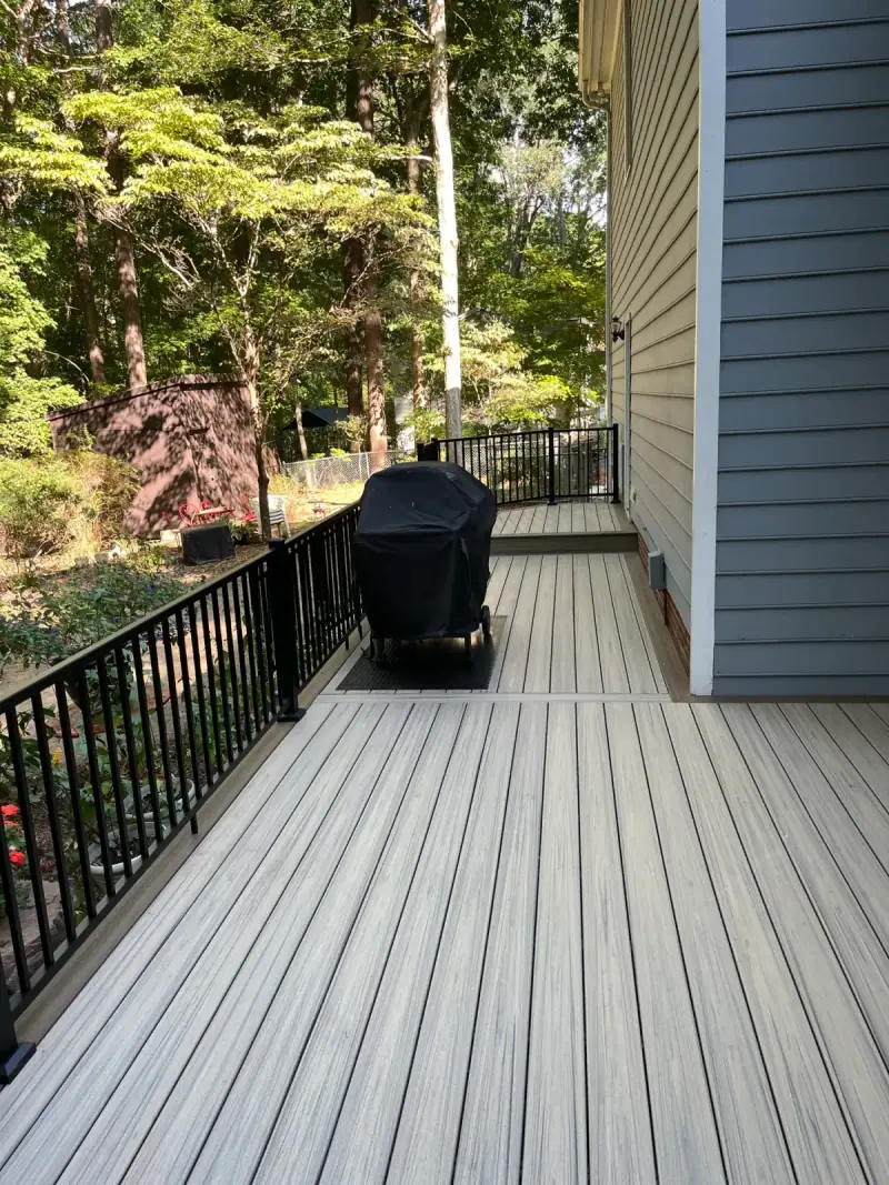 Composite deck with black railing and a grill station beside the house