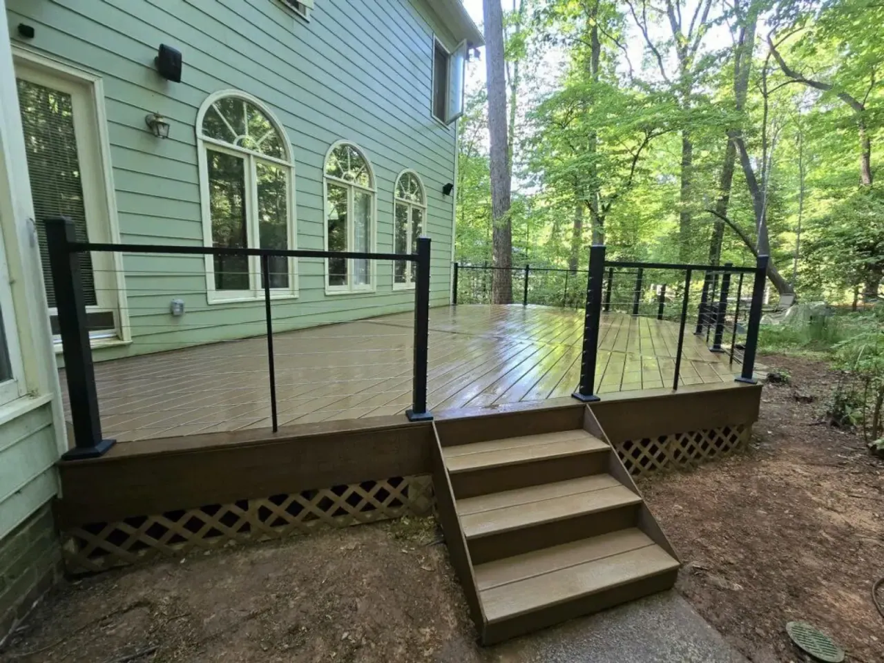 Wood deck and stairs with black railing on a green-sided Triangle home