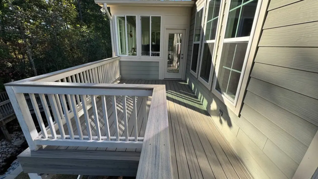Deck corner with white railing meeting the home’s bay windows