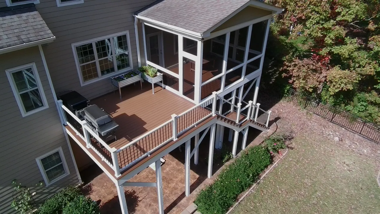 Aerial view of a screened porch and brown composite deck with white railing and stairs to the lawn