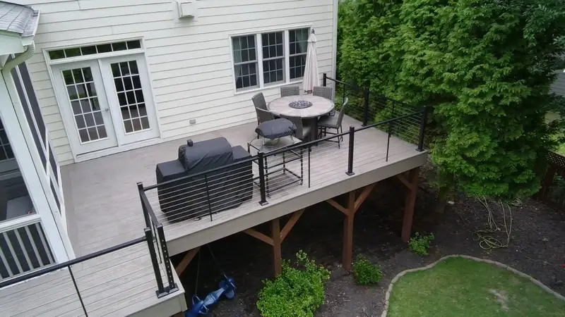 Composite deck with black railing, a grill station and a fire-table dining set, raised on timber posts above a lawn